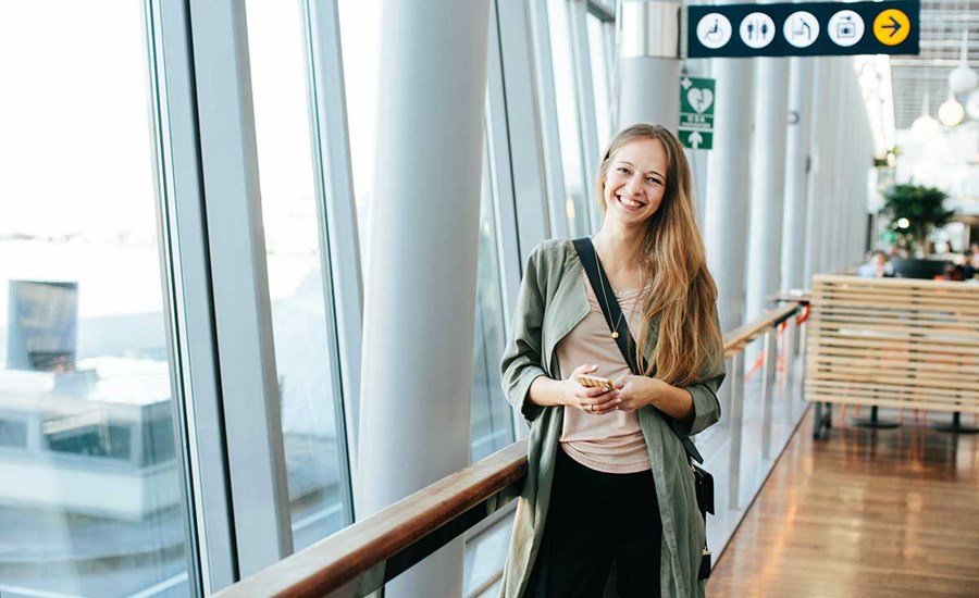 Jente står på flyplassen med mobilen i hånda, til illustrasjon for mobilbank