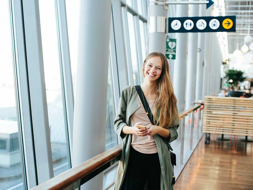 Jente står på flyplassen med mobilen i hånda, til illustrasjon for mobilbank