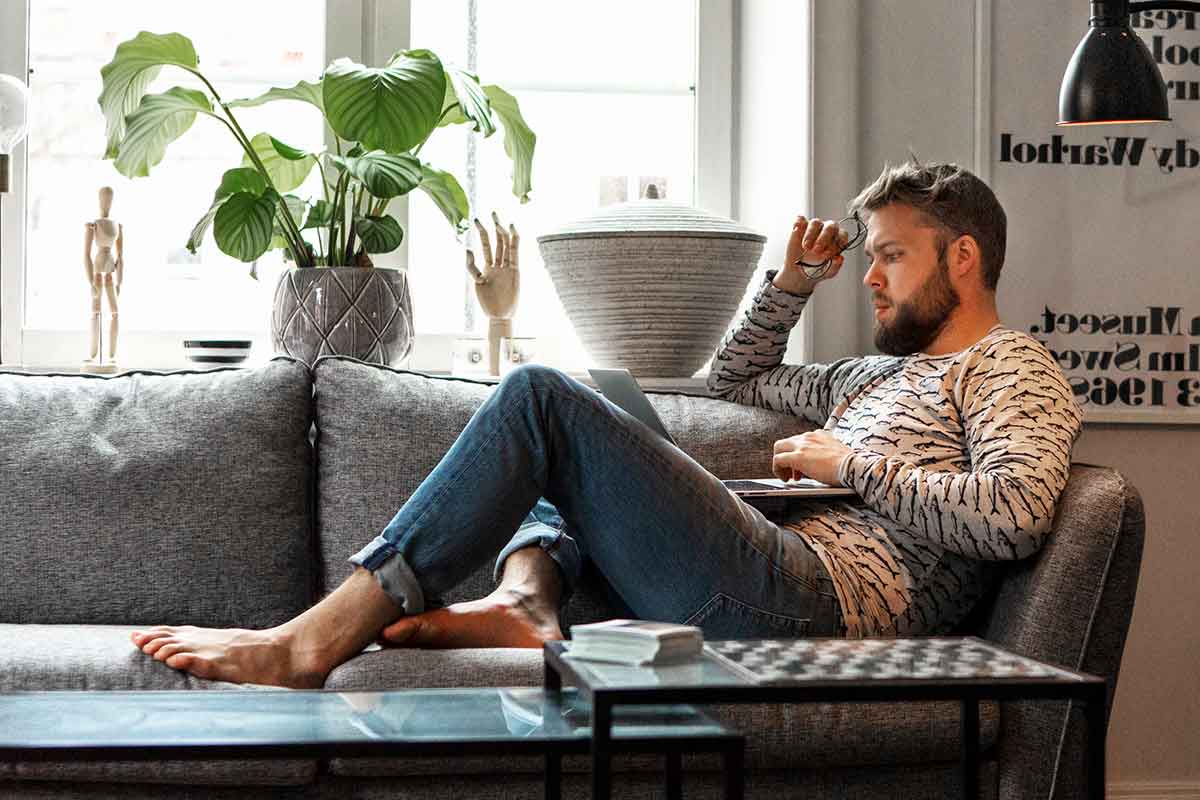 Mann sitter på sofaen og ser på laptop, til illustrasjon for nettbank