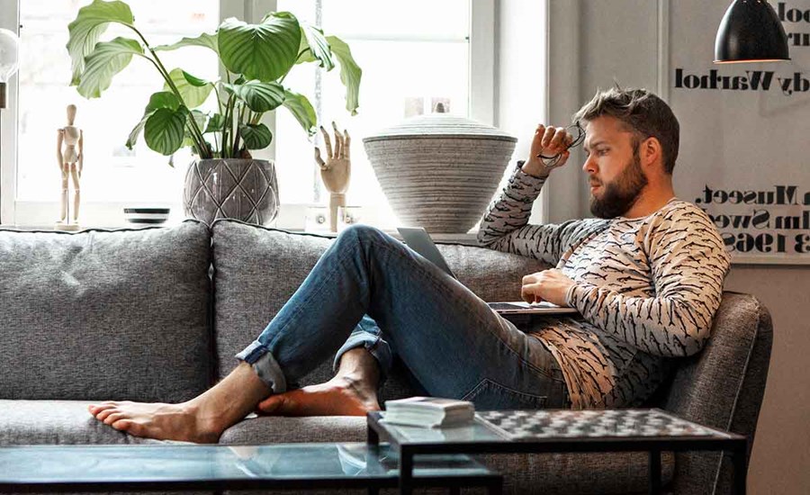 Mann sitter på sofaen og ser på laptop, til illustrasjon for nettbank