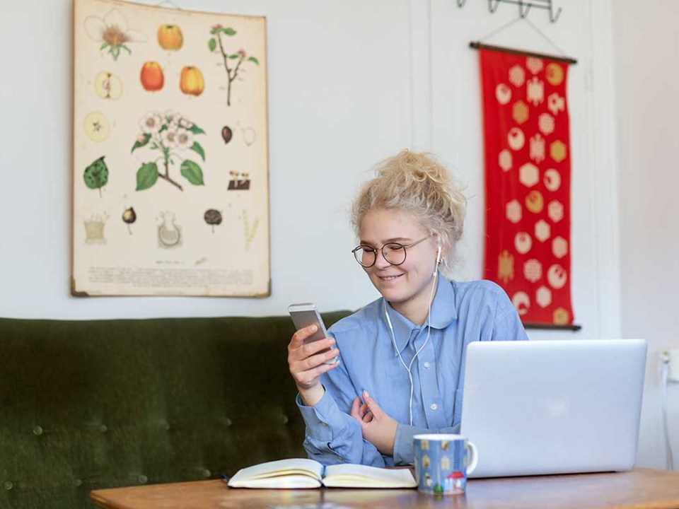 Jente sitter i grønn sofa og ser på mobilen med hodetelefoner, til illustrasjon for husleiekontrakt