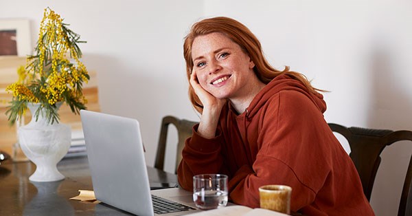 Ung jente sitter på kjøkkenbord med datamaskin fremfor seg og smiler, til illustrasjon for sparekalkulator