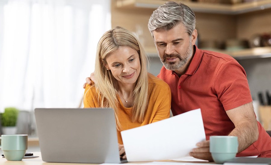 Kvinne og mann står på kjøkkenet med PC på bordet og dokument i handa, til illustrasjon for lånetyper