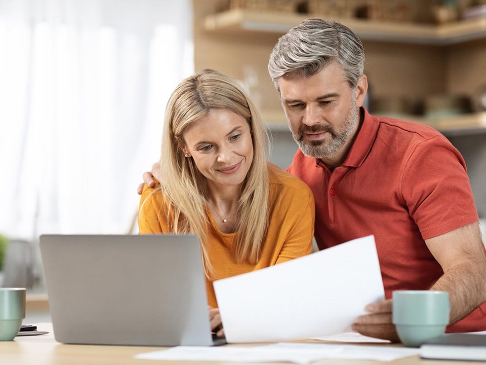 Kvinne og mann står på kjøkkenet med PC på bordet og dokument i handa, til illustrasjon for lånetyper