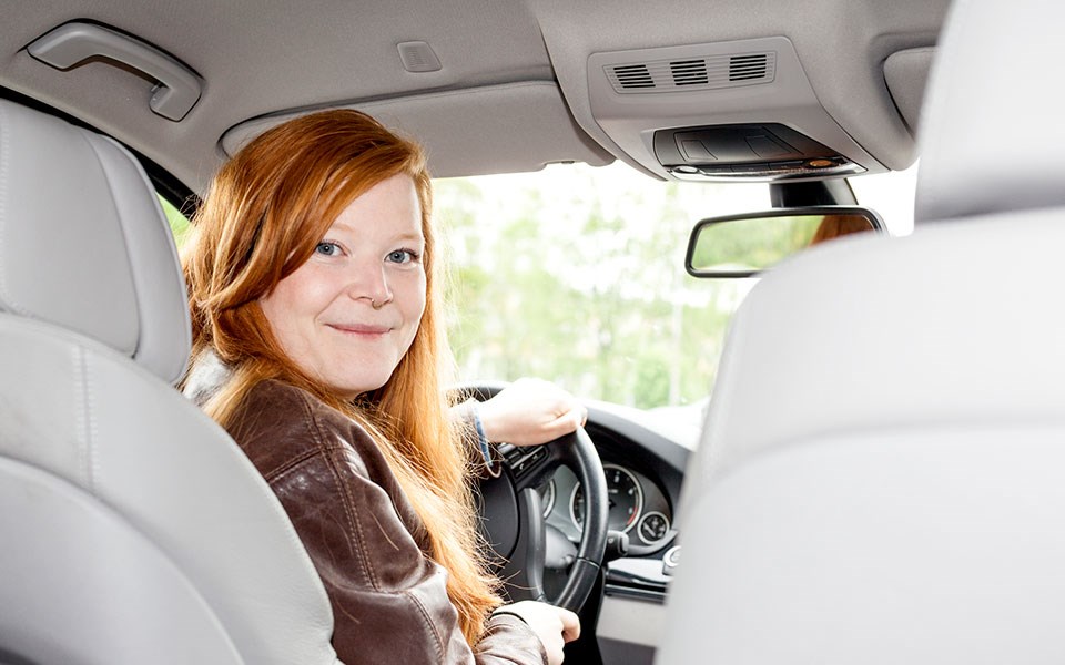 Jente sitter i bil og holder i rattet, til illustrasjon for kjøpe eller lease bil