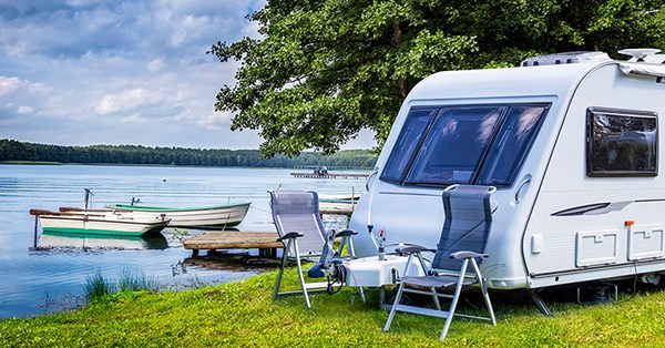 Campingvogn og campingstoler på en landlig plass med innsjø og båter, til illustrasjon for campingvognlån