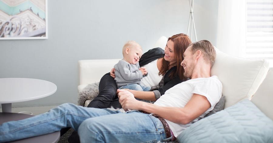 En familie på tre sitter i sofaen. Til illustrasjon for å kontakt banken om lån