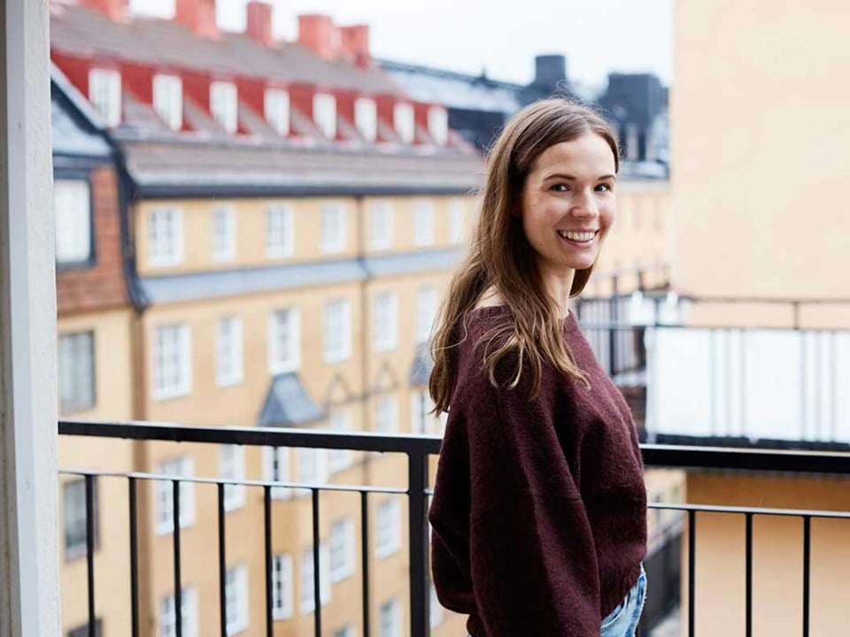Ung jente står på en balkong og smiler, til illustrasjon for førstegangskjøp av bolig