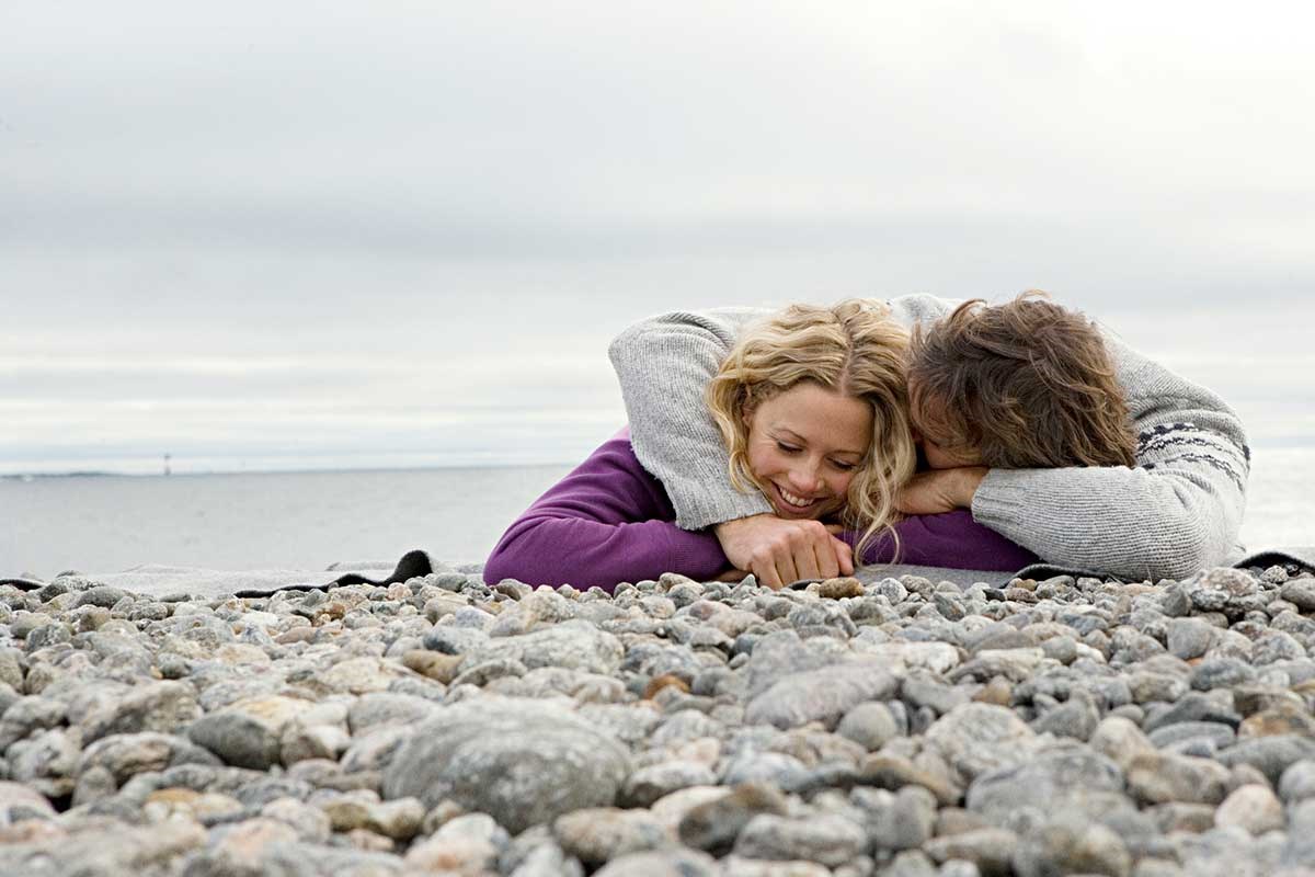 Par ligger på stranda og ler, til illustrasjon for å kjøpe seg inn i bolig