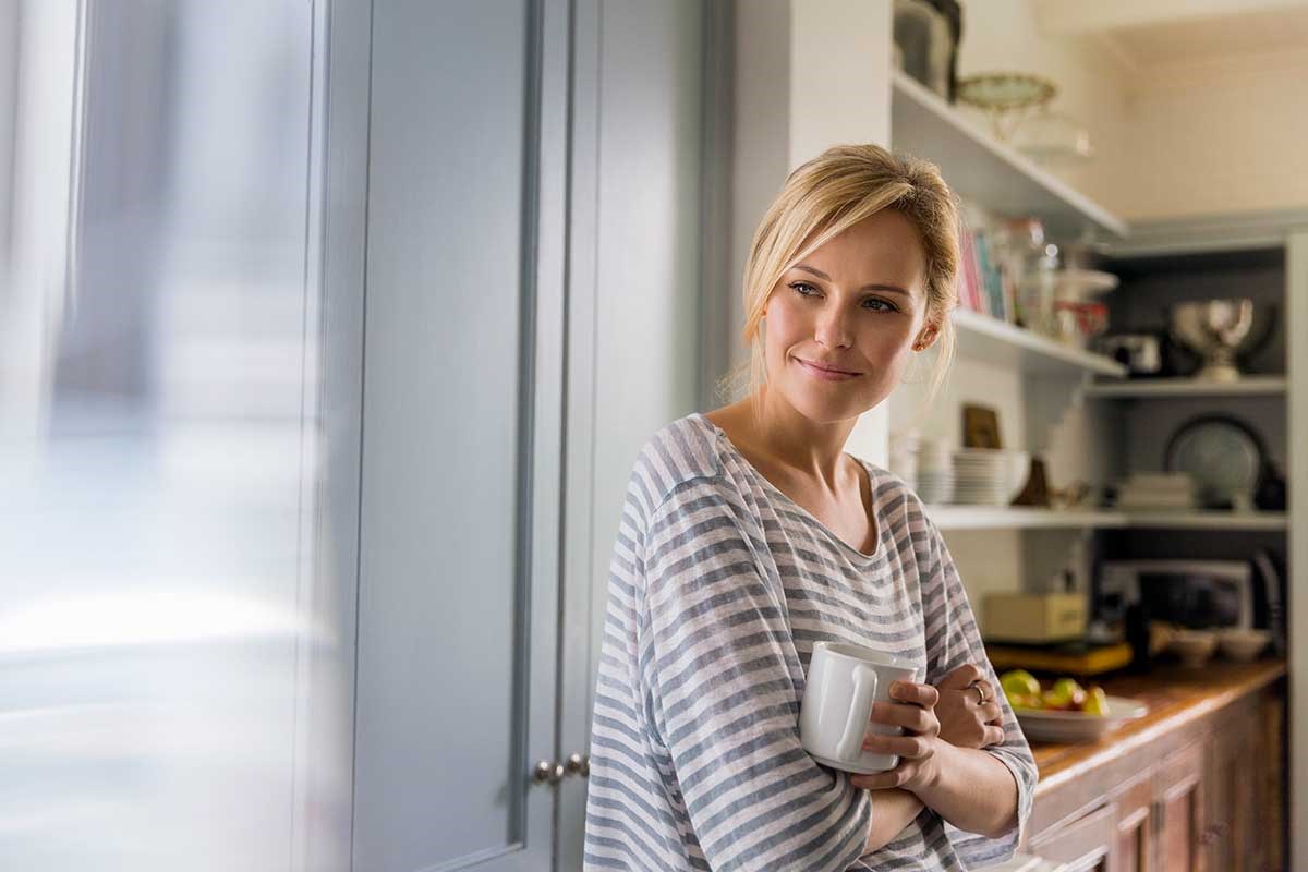Kvinne står på kjøkkenet og holder en kaffekopp, til illustrasjon for nedbetalingsplan