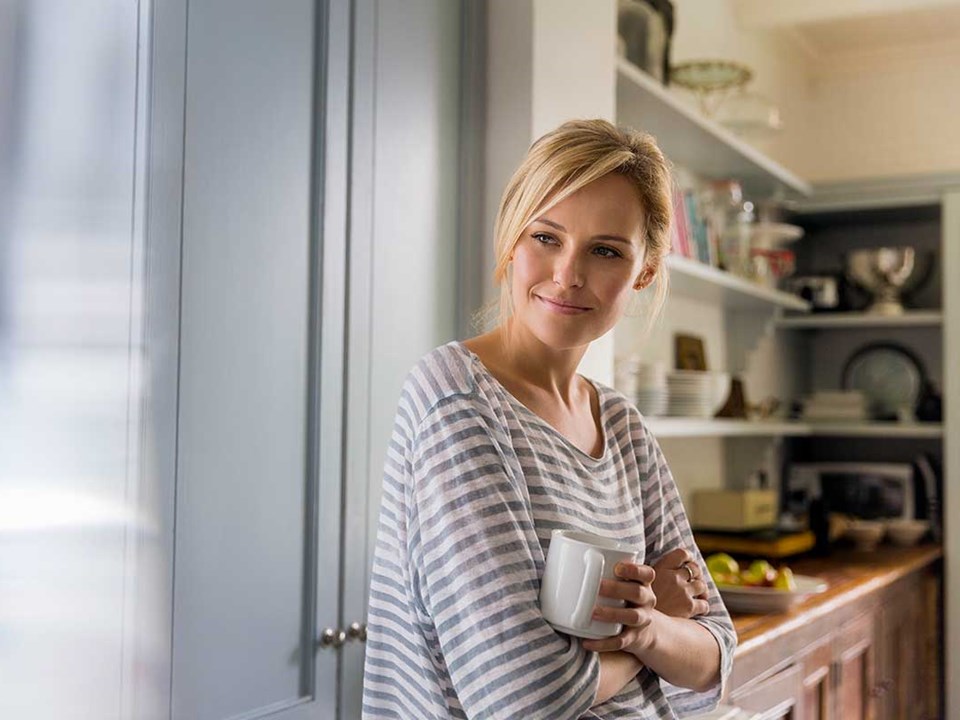 Kvinne står på kjøkkenet og holder en kaffekopp, til illustrasjon for nedbetalingsplan