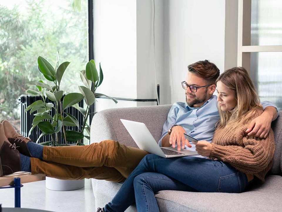 Par sitter i sofaen og ser på laptop, til illustrasjon for omkostninger ved boligkjøp