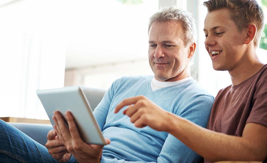 Far og sønn sitter og ser på nettbrett