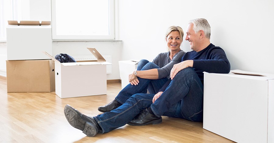 Par sitter på gulvet med flytteesker, til illustrasjon for å selge bolig