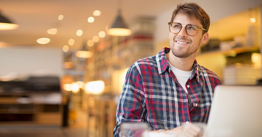 Mann med briller smiler ved pc, til illustrasjon for avdragsfrihet på boliglån
