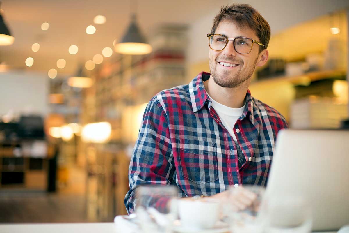 Mann med briller smiler ved pc, til illustrasjon for avdragsfrihet på boliglån