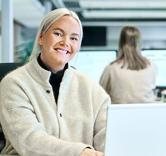 Boliglånsrådgiver Emilie sitter på kontoret og smiler med ansatte bak seg