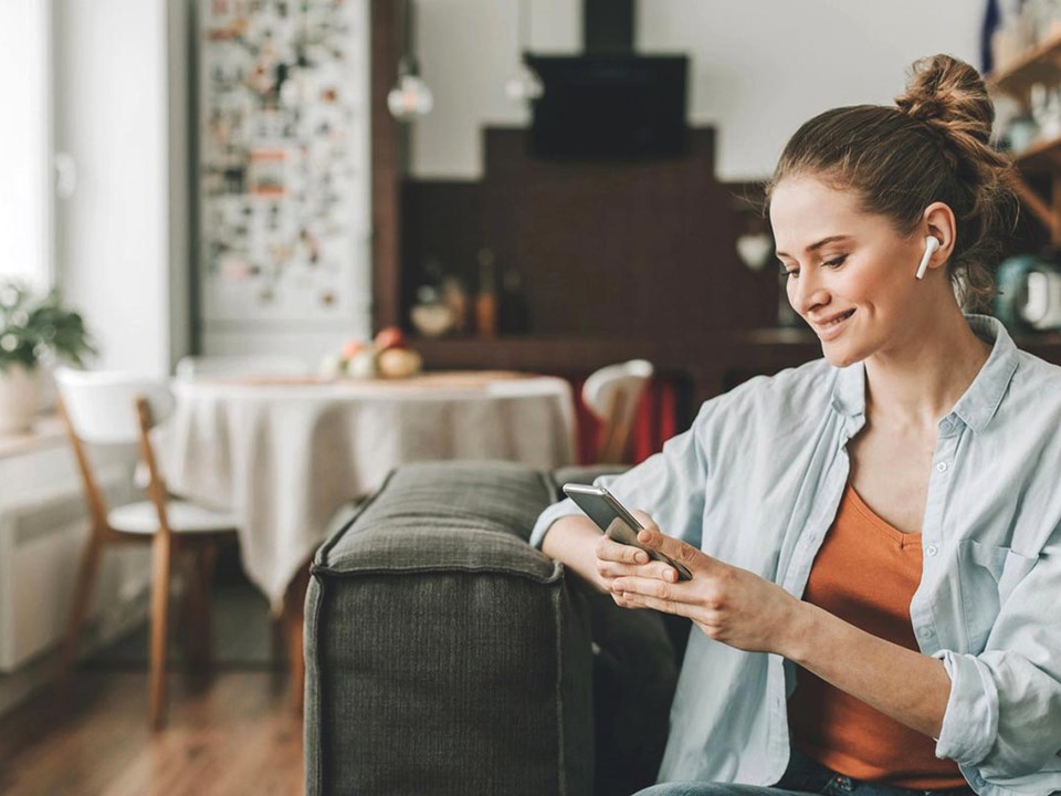 Dame sitter i en sofa med airpods i ørene og skriver på mobiltelefon, til illustrasjon for eiendomsmegler