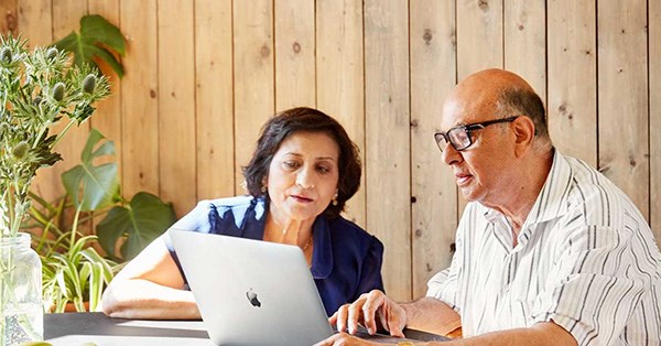 En dame og en mann sitter ved et bord og jobber med en macbook, til illustrasjon for eiendomsmegler Krogsveen