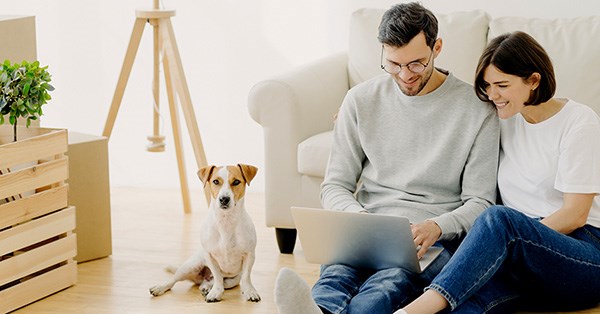 Par med hund i stua ser på laptop