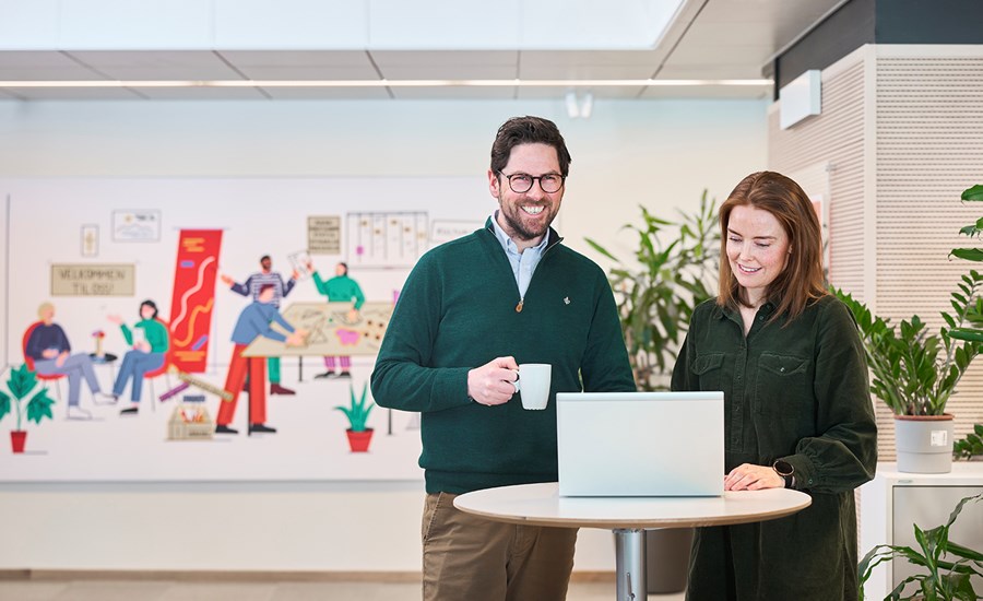 Kunderådgivere Tom og Siri jobber i BN Bank og står i lokalet med en PC og en kaffekopp, til illustrasjon for flytte boliglån