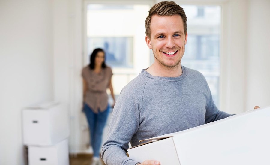 Mann står i en bolig og holder en flyttekasse, til illustrasjon for overtakelse av bolig