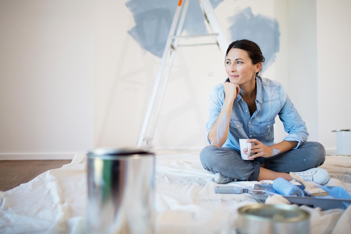 Dame sitter på gulvet i en bolig med malingsutstyr og en kaffekopp, til illustrasjon for opplåning