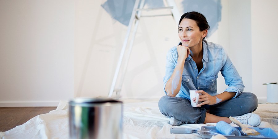 Dame sitter på gulvet i en bolig med malingsutstyr og en kaffekopp, til illustrasjon for opplåning