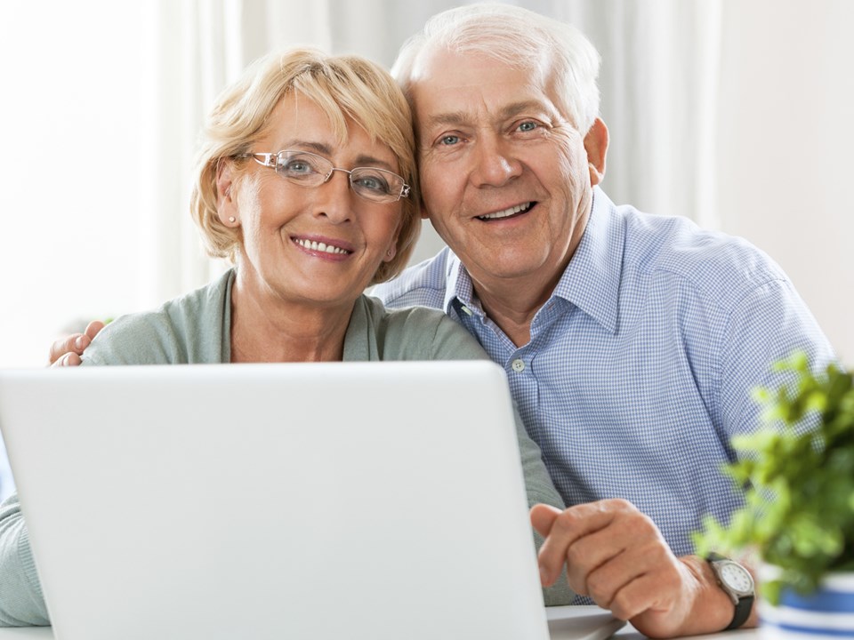 Eldre par smiler til kamera med en datamaskin fremfor seg, til illustrasjon for seniorlån
