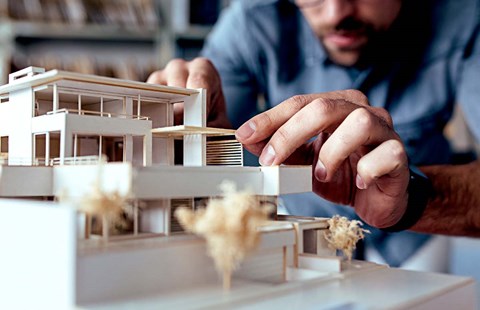 Mann leker med minivariant av et hus, til illustrasjon for å bygge på huset