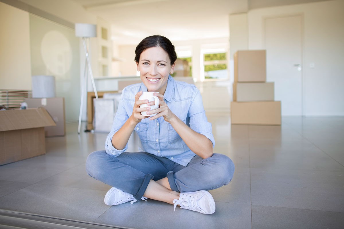 Dame sitter på gulvet i ny leilighet, illustrasjon til nye regler om kjøp og salg av leilighet
