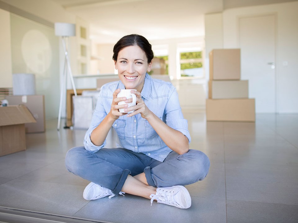 Dame sitter på gulvet i ny leilighet, illustrasjon til nye regler om kjøp og salg av leilighet