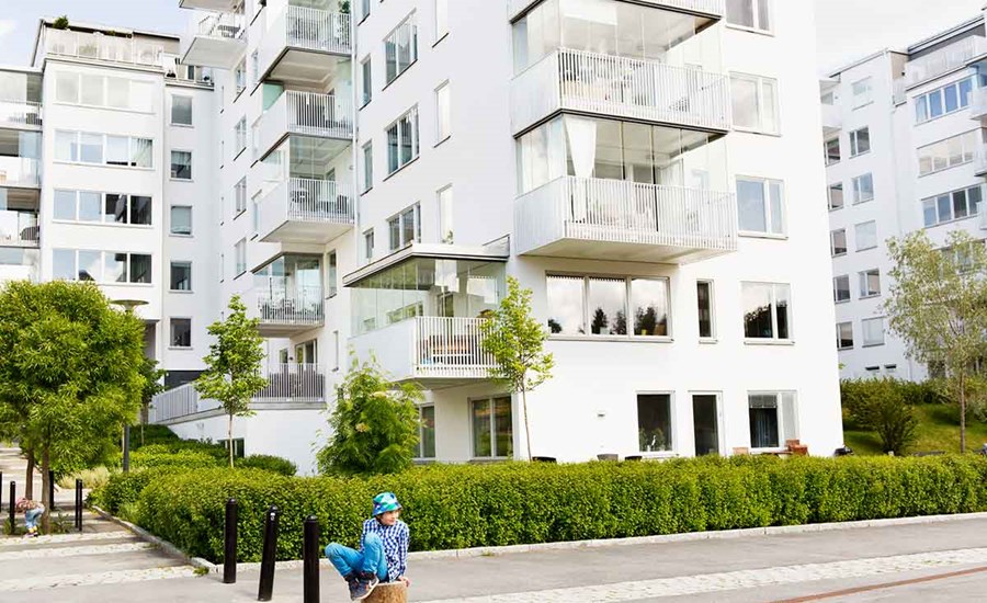 Gutt med bøttehatt sitter på en stokk fremfor en boligblokk, til illustrasjon for sekundærbolig
