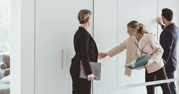 Megler viser frem bolig til en kvinne og en mann som ser på skap og holder prospet