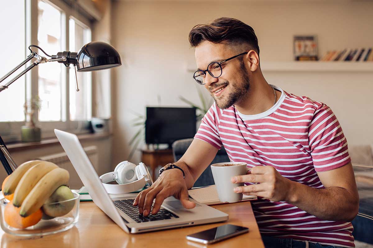 Mann sitter ved pulten med en kaffekopp i hånda og jobber på PC, til illustrasjon for hvordan beregne egenkapital