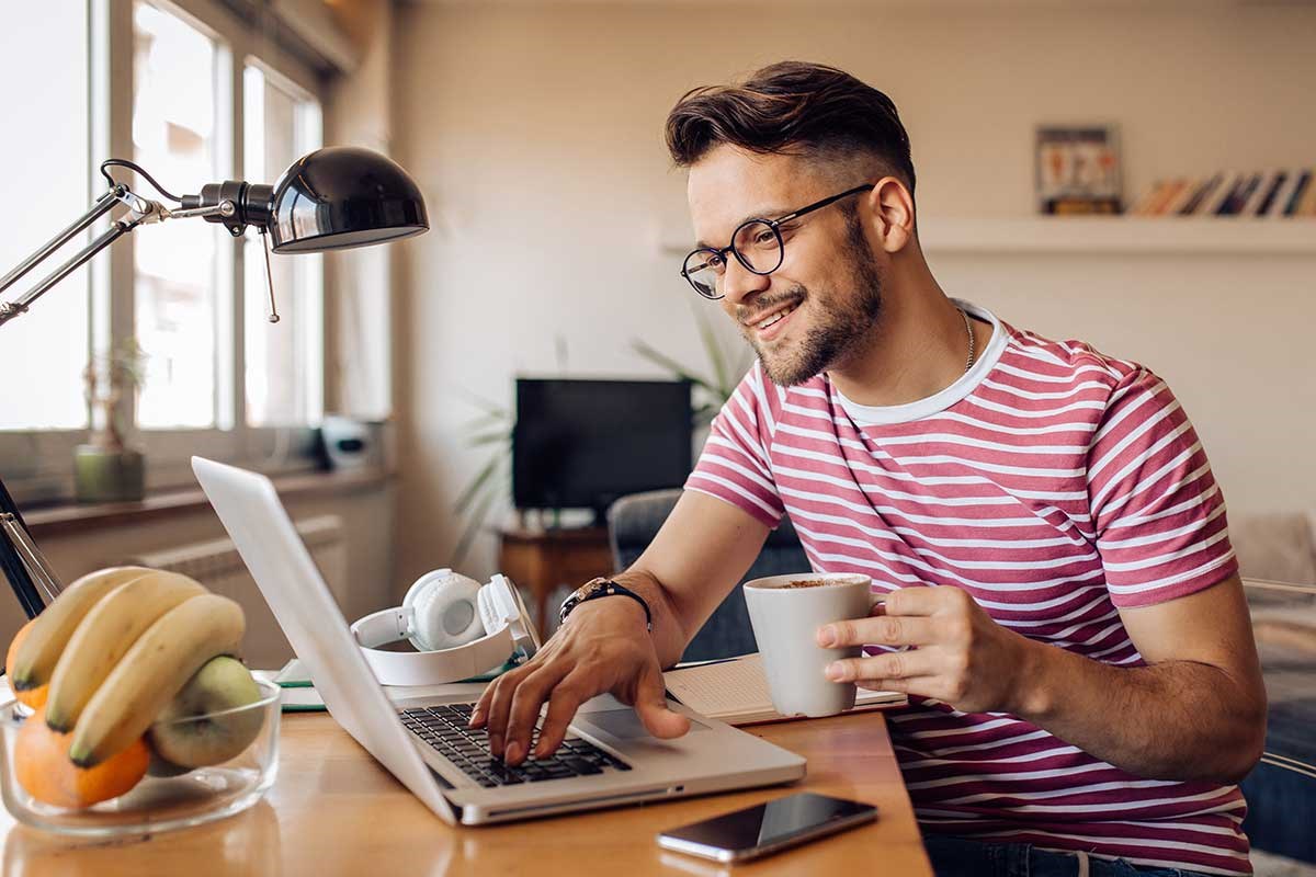 Mann sitter ved pulten med en kaffekopp i hånda og jobber på PC, til illustrasjon for hvordan beregne egenkapital