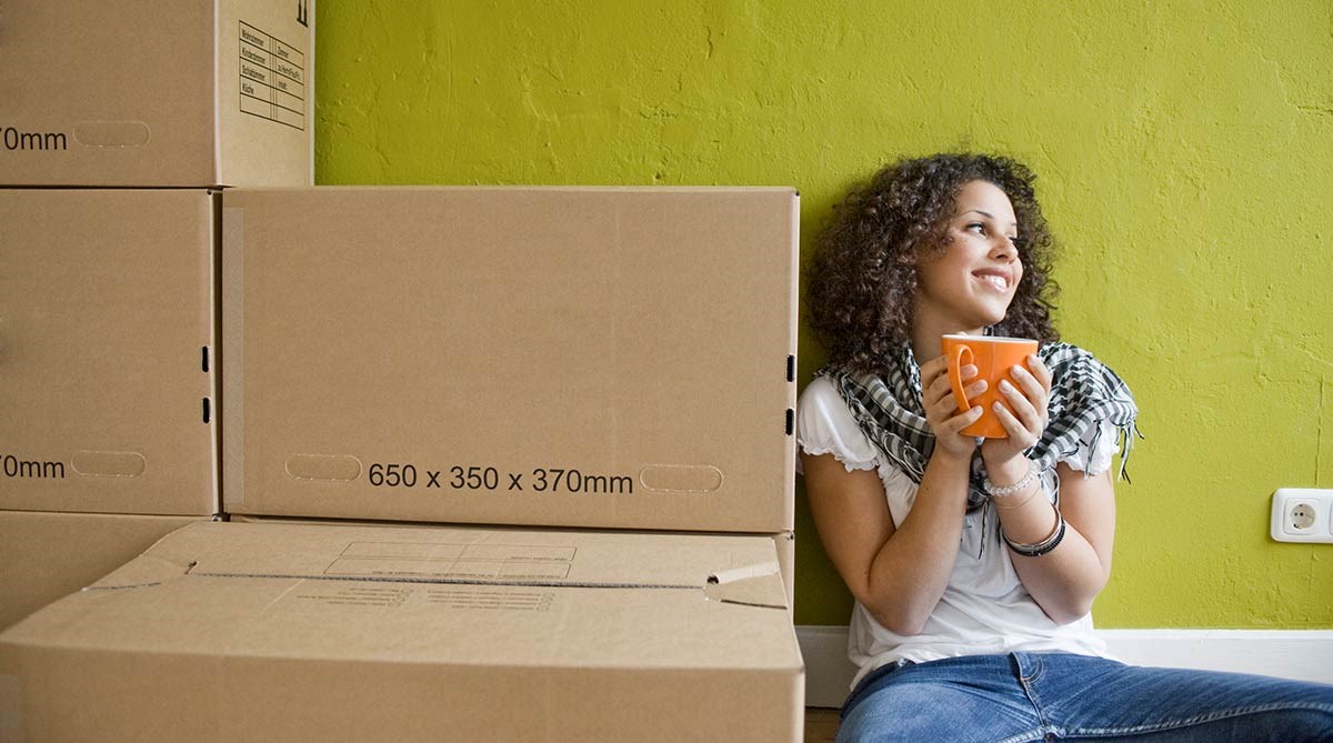 Dame sitter på gulvet og drikker kaffe med flyttekasser rundt seg, til illustrasjon for Finit deleie