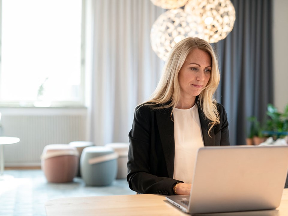 Dame sitter ved en pult og jobber på en laptop, til illustrasjon for hvor mye kan jeg kjøpe bolig for