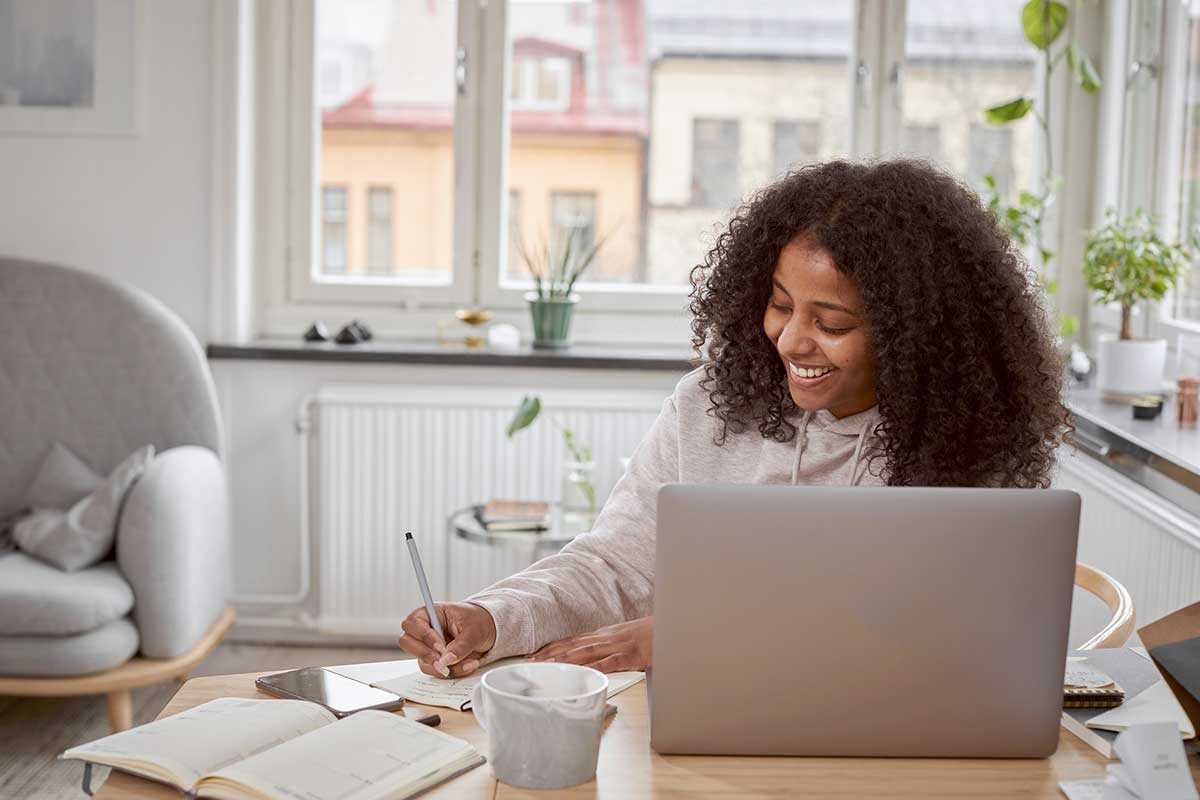 Dame sitter ved spisebord og skriver notater, til illustrasjon for refinansiere forbruksgjeld