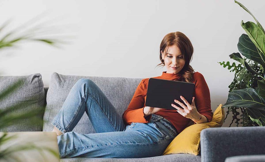 Dame sitter i sofa og leser på nettbrett, til illustrasjon for logg inn i bn bank