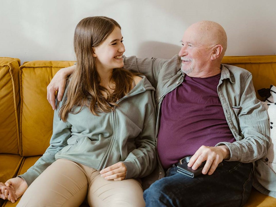 Eldre mann holder armen rundt en jente mens de sitter i en sofa, til illustrasjon for forskudd på arv