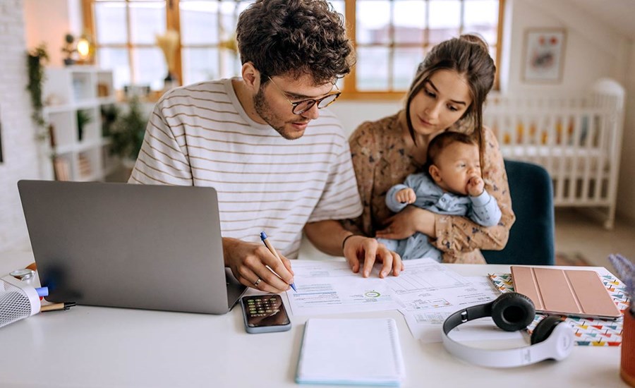 Mann jobber seg gjennom dokumenter som ligger på et bord med en kvinne og en baby vedsiden av, til illustrasjon for økonomiske problemer