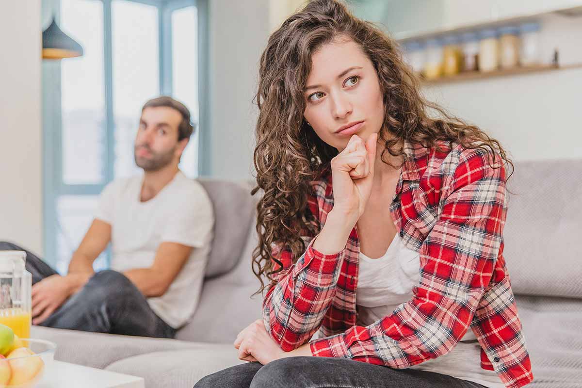 Dame i rutet skjort og mann i bakgrunnen sitter og tenker, illustrasjon til samlivsbrudd og økonomi