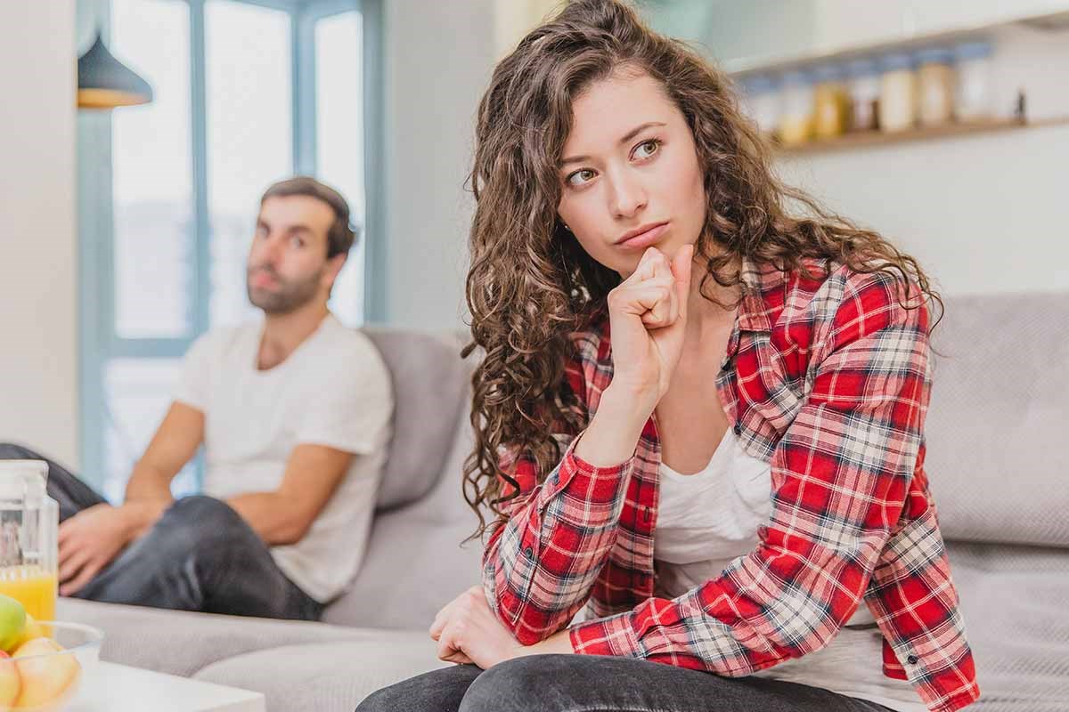 Dame i rutet skjort og mann i bakgrunnen sitter og tenker, illustrasjon til samlivsbrudd og økonomi