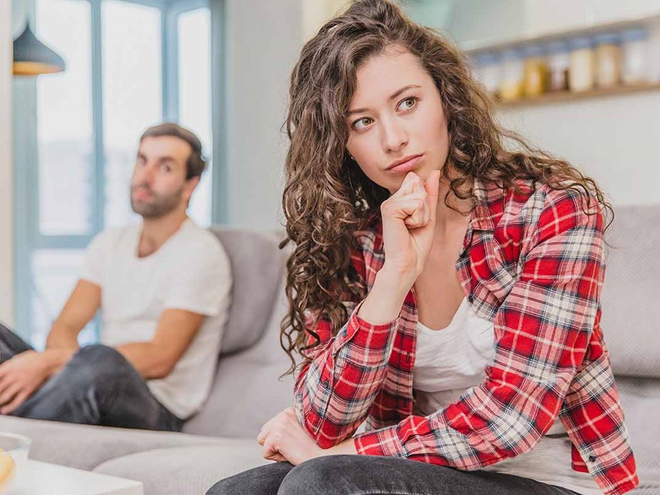 Dame i rutet skjort og mann i bakgrunnen sitter og tenker, illustrasjon til samlivsbrudd og økonomi