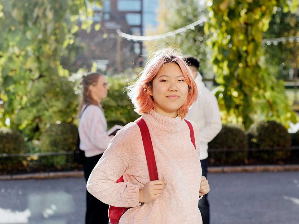 Jente med rosa hår står ute med en rød skolesekk, til illustrasjon for studentbudsjett