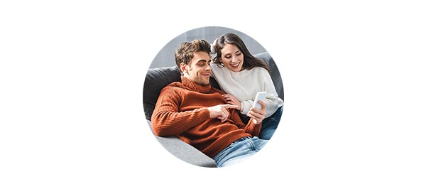 Mann og kvinne sitter i sofaen og sjekker felleskonto på mobil