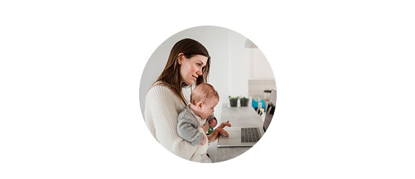 Kvinne holder baby og sjekker regningskontoen på PC