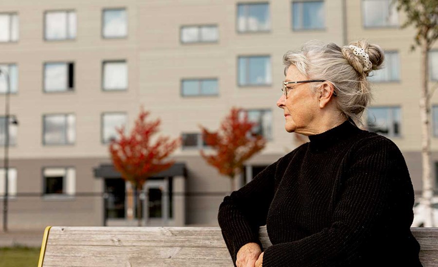 Eldre kvinne sitter på en benk utenfor en boligblokk, til illustrasjon for økonomi for eldre