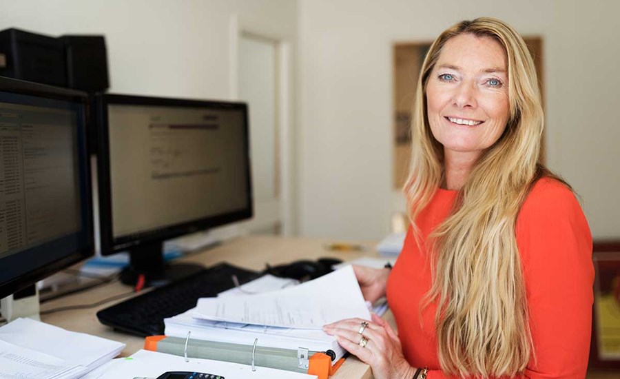 Kvinne sitter ved en pult med en stor bok med dokumenter for å få kontroll på økonomien